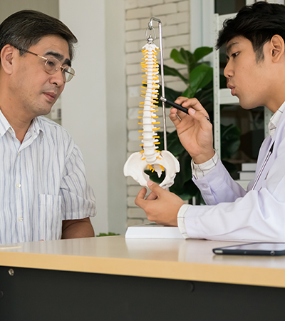 Chiropractor pointing at spine bone model, explaining the problem to mature female patient.