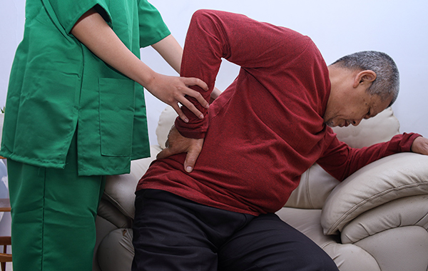 Red-T-shirt-Elderly-Man-Trying-to-Get-Up-from-the-Sofa-with-the-Help-of-Chiropractor-NoFrills-Chiropractic-Singapore