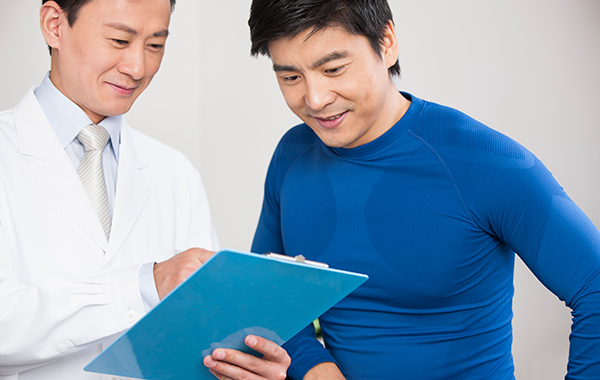 Male-Chiro-with-male-patient-looking-at-report-NF-Chiropractic Male-White-Coat-Explaining-Xray-to-Patient-Sitting-Next-to-Him-NoFrills-Chiropractic-Singapore