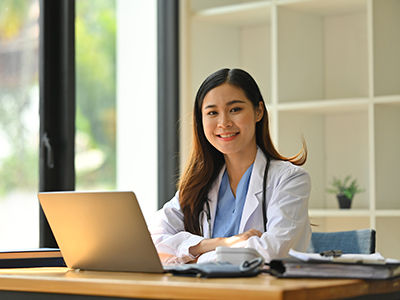 lady-chiropractor-sitting-on-the-table-NF-Chiropractic Female-Chiropractor-Sitting-Down-on-a-Desk-Smiling-NoFrills-Chiropractic-Singapore