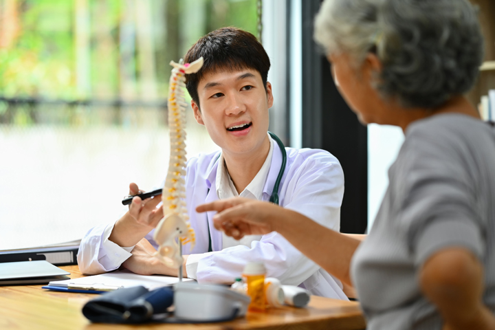 Male chiropractor explaining structure of spine to mature female patient in clinic. Health care concept.