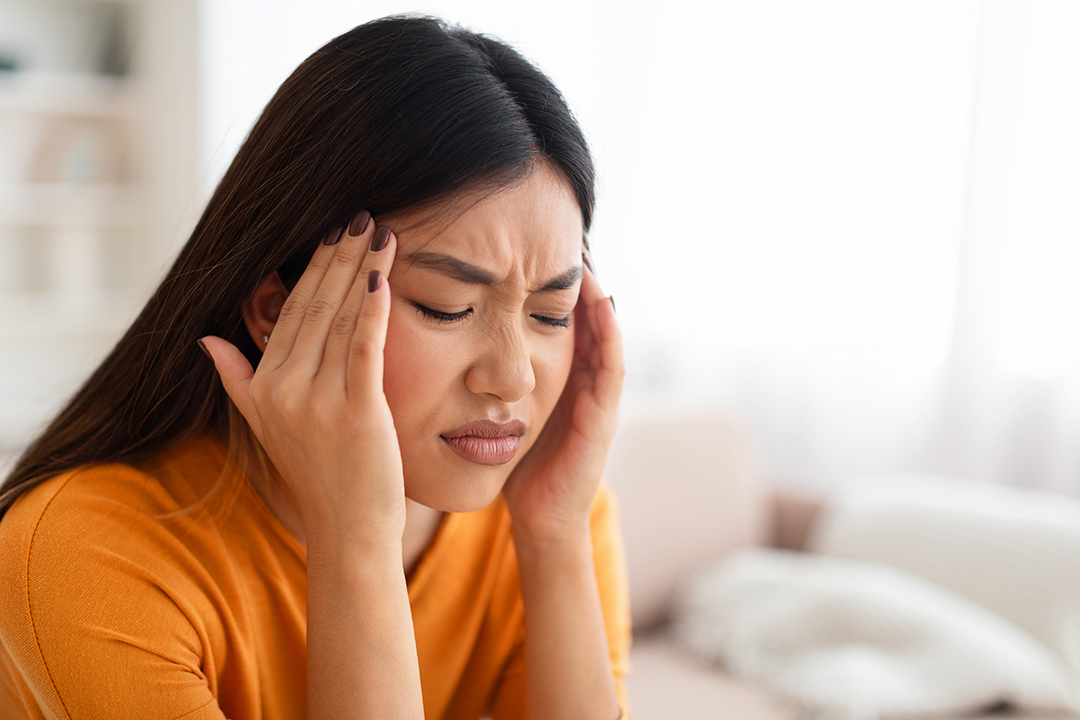 Closeup of unhappy young asian lady touching her head Female-Chiro-touching-lower-back-NF-Chiropractic
